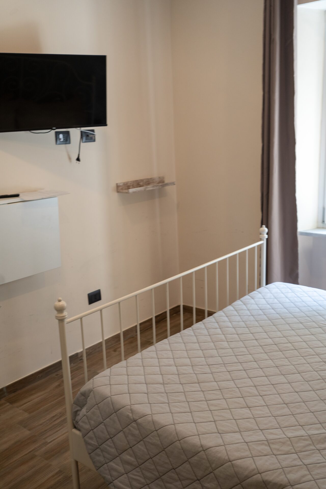 Camera matrimoniale con TV a parete, mensola e letto in ferro battuto